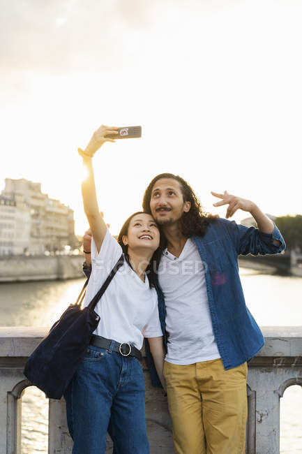 France, Paris, happy young couple taking a selfie at river Seine at sunset — Stock Photo