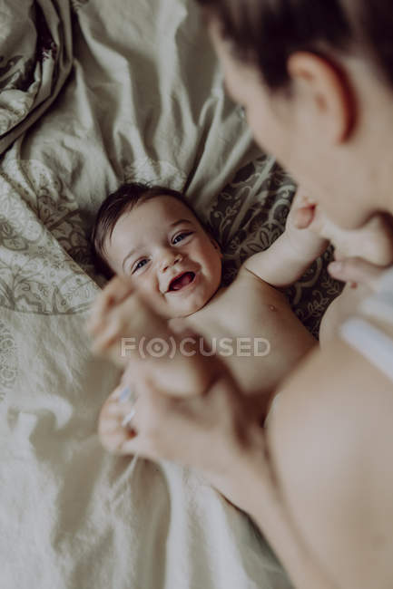 Mother playing with cheerful baby son in bed — brown hair, Mid Adult -  Stock Photo | #268648520