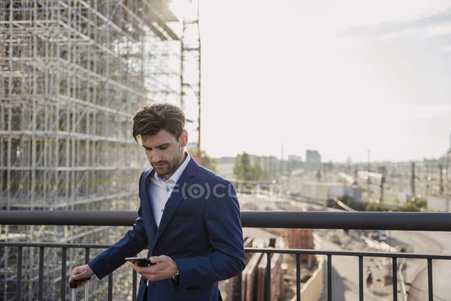 Бизнесмен, стоящий на мосту в городе с помощью мобильного телефона — стоковое фото