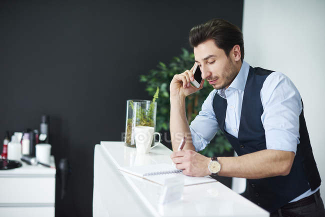 Hairdresser talking on cell phone checking diary — Stock Photo