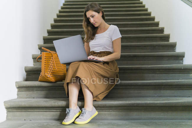 Mujer sentada en una escalera usando laptop - foto de stock