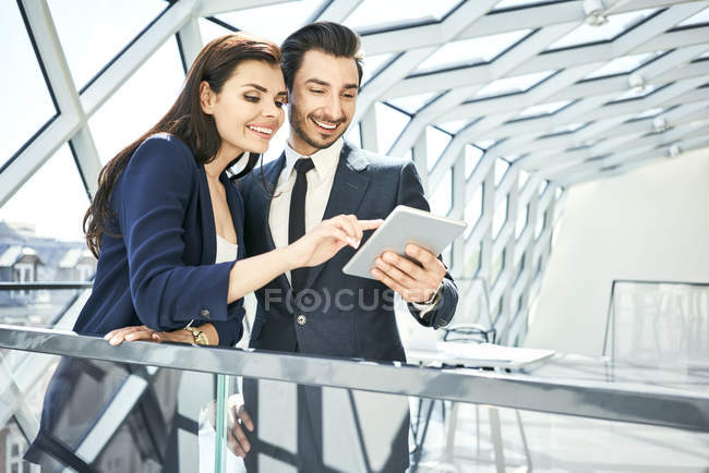 Empresaria y hombre de negocios compartiendo tableta en la oficina moderna - foto de stock