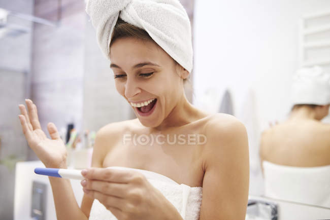 Портрет збудженої молодої жінки дивлячись на вагітність випробування у ванній — стокове фото