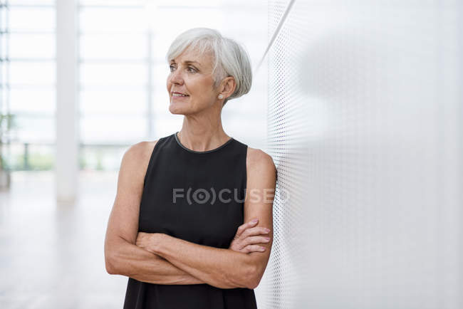 Старша жінка в чорному одязі, спираючись на стіну і дивлячись боком — стокове фото