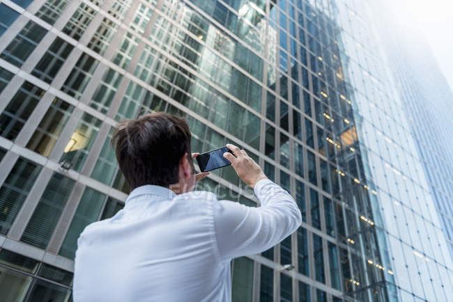 Businessman taking cell phone picture of skyscraper — Stock Photo