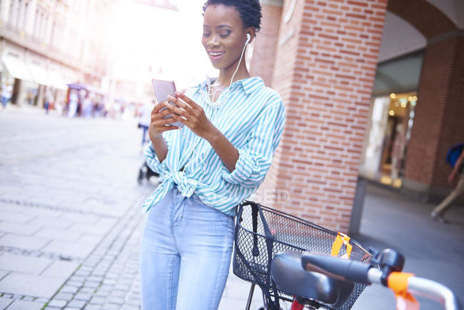 Портрет улыбающейся женщины с наушниками и сотовым телефоном в городе — стоковое фото