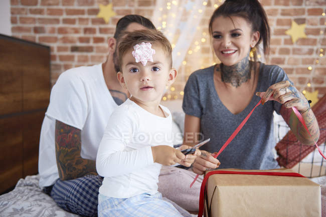 Retrato de niño abriendo regalo de Navidad con sus padres en la cama — Stock Photo