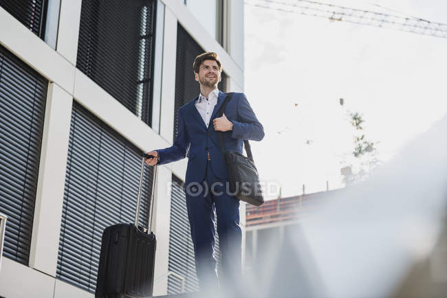 Smiling businessman with baggage in city looking around — Stock Photo