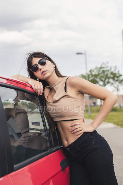 Portrait of young woman wearing sunglasses leaning on car — Stock Photo