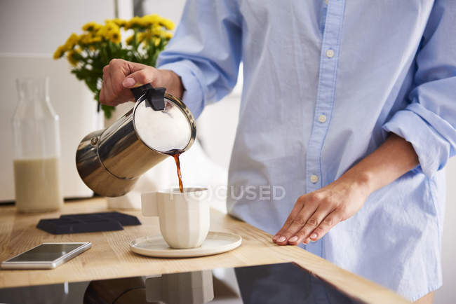 Молодая женщина наливает кофе в чашку, обрезанный образ — стоковое фото