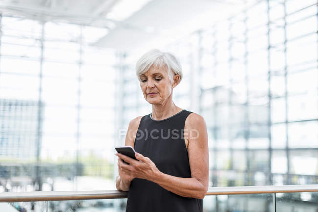 Seniorin steht am Geländer und benutzt Handy — Stockfoto
