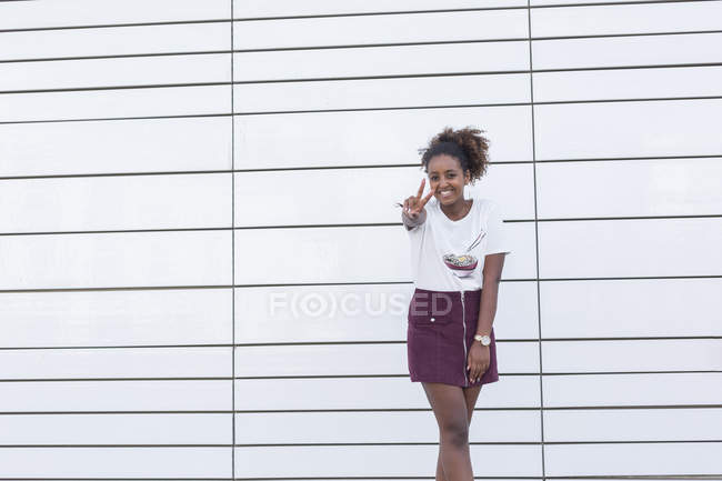 Ritratto di giovane studentessa afro-americana sorridente che gesticola il segno della pace con le dita sulla macchina fotografica — Foto stock