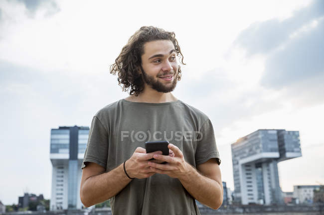 Улыбающийся молодой человек держит мобильный телефон и смотрит в сторону — стоковое фото