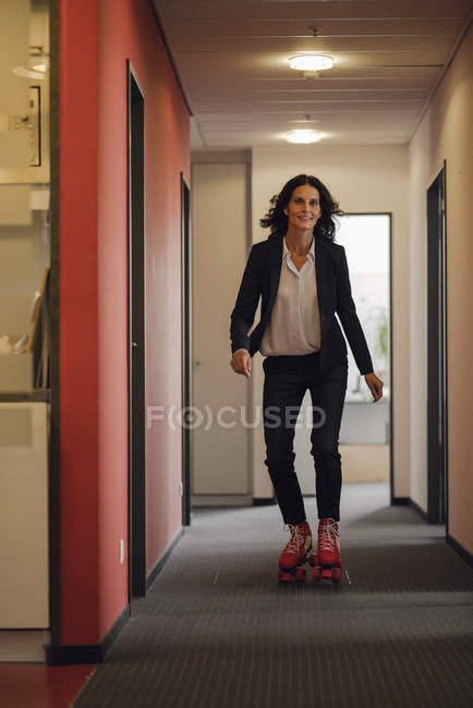 Madura mujer de negocios patinaje sobre ruedas en corredor de oficinas — Stock Photo