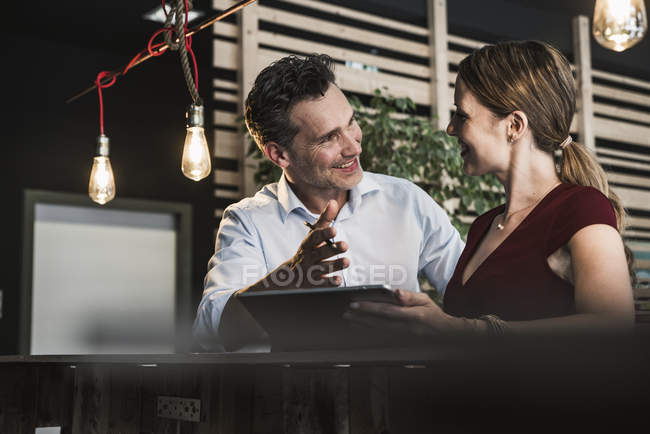 Mujer de negocios sonriente y hombre de negocios con tableta discutir en la oficina - foto de stock