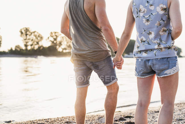 Giovane coppia che cammina a riva del fiume tenendosi per mano — Foto stock