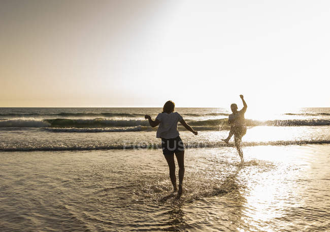 Jovem casal se divertindo na praia, salpicando água no mar — Fotografia de Stock