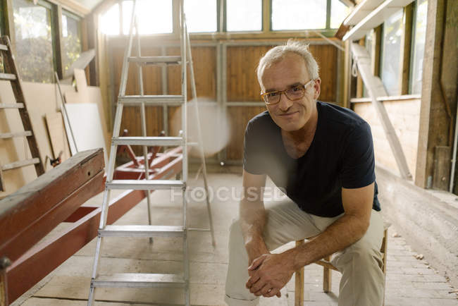 Portrait of confident mature man sitting in workshop — Stock Photo