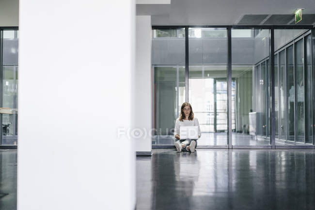 Businesswoman sitting on ground in empty office and using laptop — Stock Photo