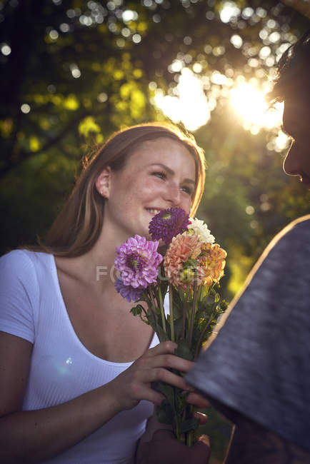 Jeune homme rencontrant sa petite amie dans un parc, lui offrant des fleurs — Photo de stock