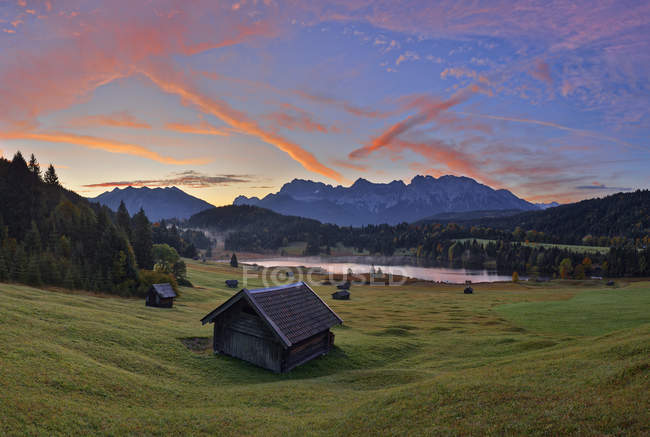 Alemanha, Baviera, Werdenfelser Land, lago Geroldsee com celeiro de feno ao pôr do sol, no fundo as montanhas Karwendel ao nascer do sol — Fotografia de Stock