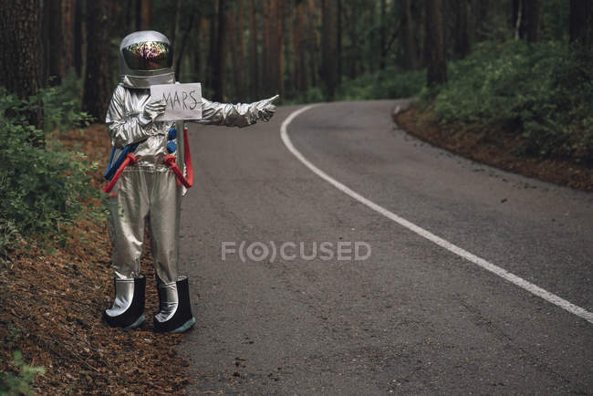 Spaceman hitchhiking to Mars, standing on road in forest — Stock Photo