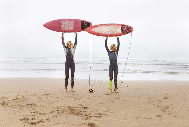 Испания, Авилес, двое подростков-серферов на пляже, держащих доски для серфинга на плаву — стоковое фото
