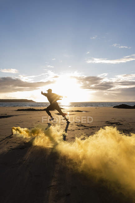 Uomo che fa movimento di formazione in spiaggia con fumo colorato al tramonto — Foto stock