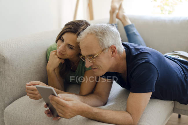 Усміхнена Зріла пара лежачи на дивані на домашній планшет — стокове фото