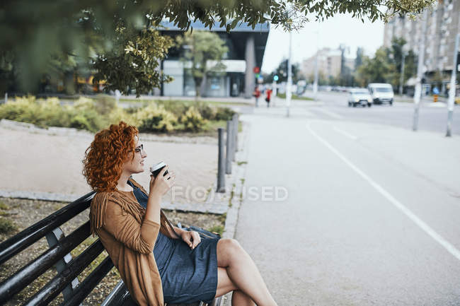 Jovem mulher sentada em um banco, bebendo café — Fotografia de Stock
