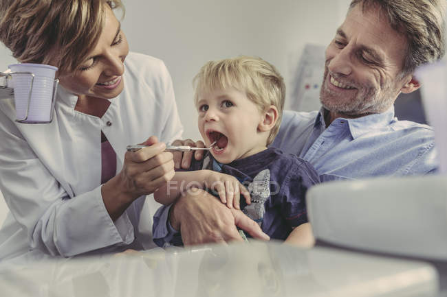 Odontoiatra esaminando bambino, seduto sulle ginocchia di suo padre — Foto stock