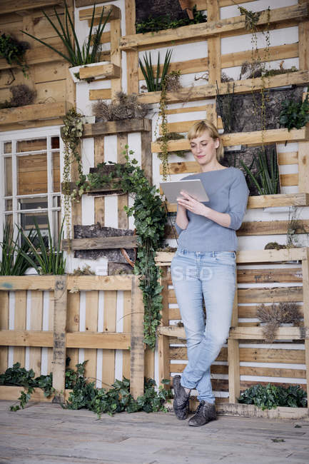 Mujer usando tableta delante de estantes de madera con plantas de interior - foto de stock