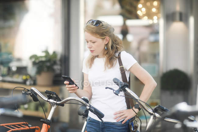 Alemanha, jovem com smartphone alugando uma bicicleta da cidade — Fotografia de Stock