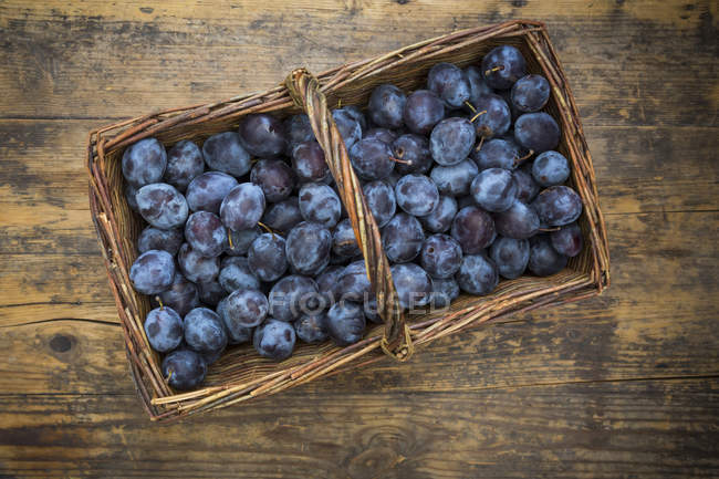 Wicker basket of organic plums, wooden table — Stock Photo
