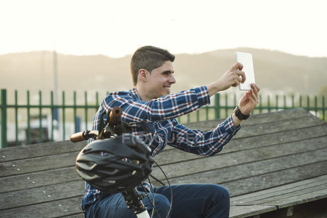 Jeune homme souriant avec vélo prenant selfie avec une tablette — Photo de stock