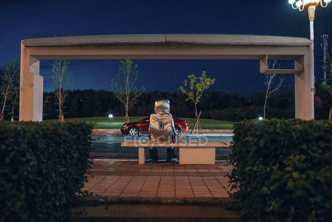 Raumfahrer sitzt nachts auf Bank an Bushaltestelle — Stockfoto