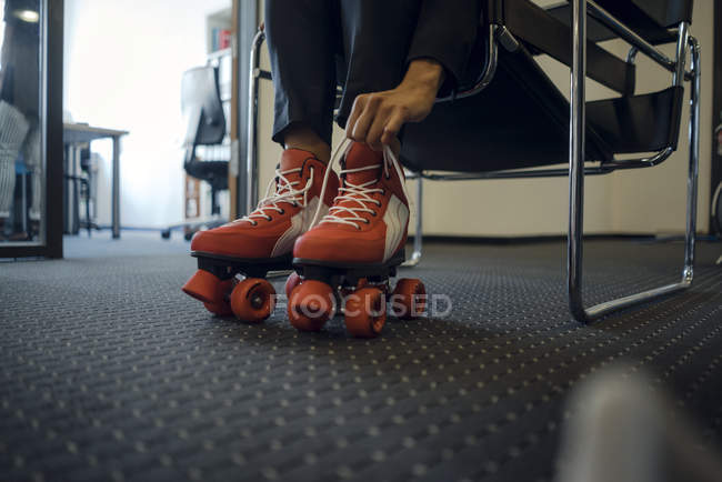 Частичный взгляд деловой женщины, сидящей в офисном коридоре, надевающей роликовые коньки на ноги — стоковое фото