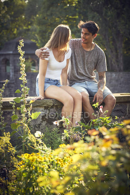 Romantico giovane coppia seduta sul muro in un parco, con le braccia intorno — Foto stock