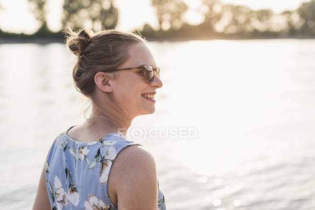 Sorrindo jovem mulher na ensolarada margem do rio — Fotografia de Stock