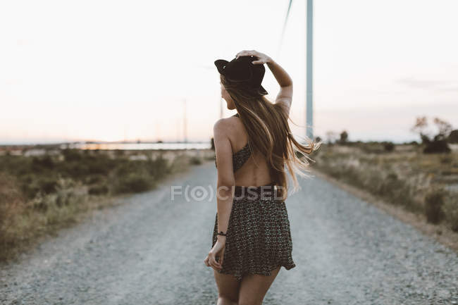 Rückansicht einer jungen Frau, die abends auf einer Landstraße läuft — Stockfoto