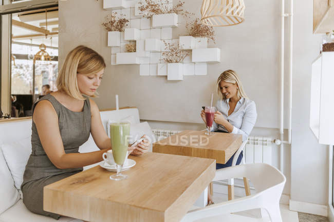 Two young women using smartphones in a cafe — Stock Photo
