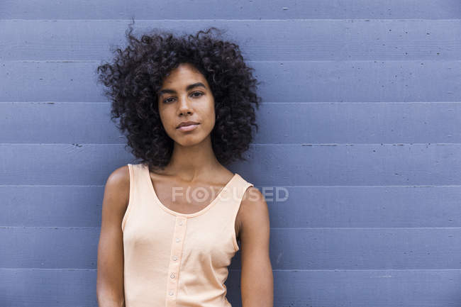 Портрет молодої жінки з кучерявим чорним волоссям, що спирається на стіну — стокове фото