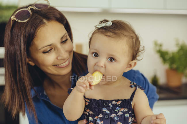 Madre viendo bebé hija comiendo una manzana - foto de stock