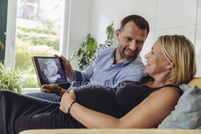 Зріла вагітна пара дивиться 3D зображення своєї майбутньої дитини на планшетний комп'ютер — стокове фото