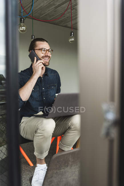 Smiling young businessman on cell phone in office — Stock Photo