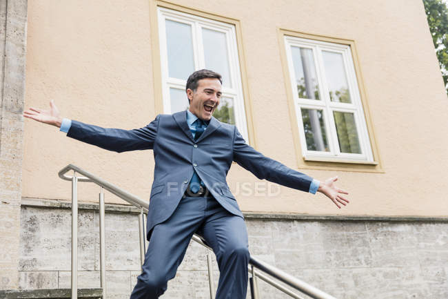 Carefree businessman sliding down railing in city — Stock Photo