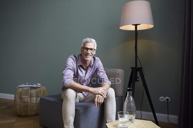 Portrait of smiling mature man sitting on armchair at home — Stock Photo