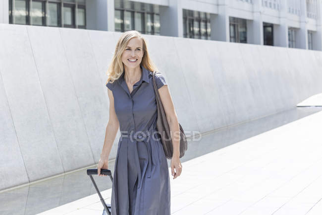 Donna d'affari bionda sorridente con bagaglio a ruote — Foto stock