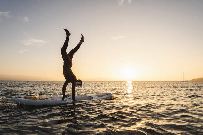 Giovane che fa stand sul paddleboard al tramonto — Foto stock