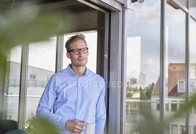 Giovane con tazza di caffè in piedi alla porta del balcone — Foto stock